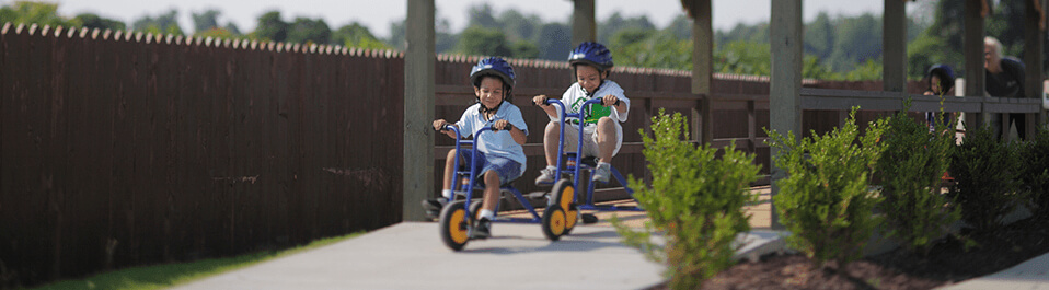 Kids riding tricycles down a paved trail.